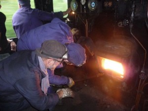 Le chauffeur "titulaire" (en noir) indique au chauffeur "en formation" les zones où il manque du charbon.